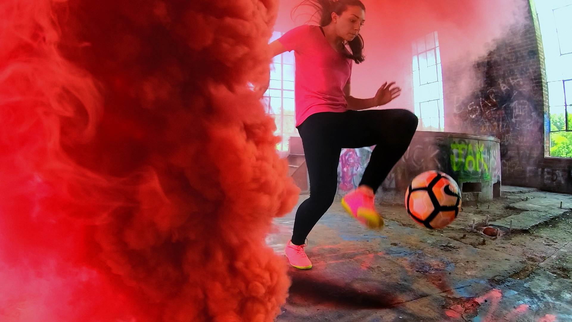 A girl does soccer tricks with colored smoke around her.